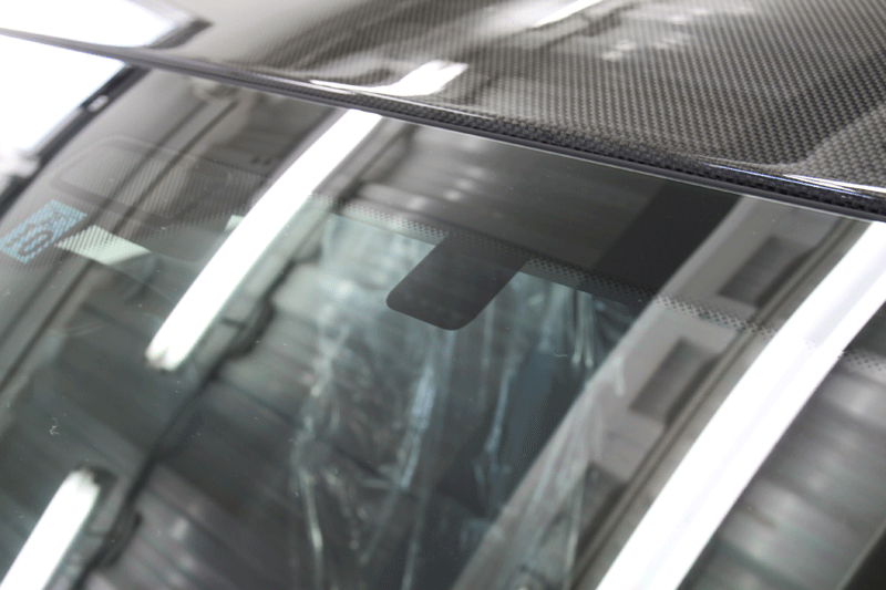 フロントガラス上部にドライブレコーダーの土台部分のフィルム施工の様子。 width=